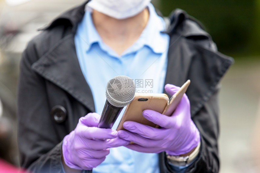 记者佩戴保护手套和面罩防冠状新冠19疾病在毒流行期间用麦克风进行媒体采访图片