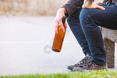 一个人在户外的长椅上喝着酒瓶子一个人在户外的长凳上喝着酒瓶子背景图片