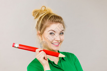 金发女学生或教师拿着大红铅笔工作室拍摄在灰色上微笑的女人手握着大铅笔图片