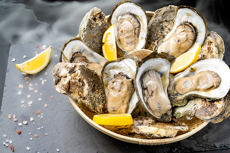 新鲜的牡蛎在黑石板上的篮子里塞柠檬新鲜的海食品和欧洲烹饪美食的概念背景图片