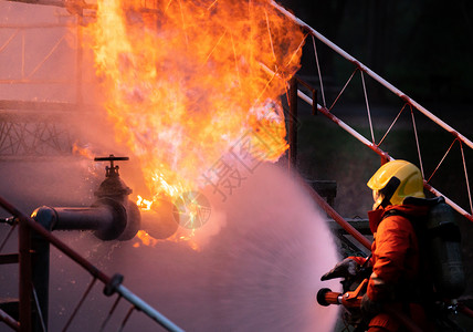 喷水消防员消防员使用水雾式灭火器与石油管道泄漏和钻机天然气站爆炸产生的火焰作斗争消防员和工业安全概念背景