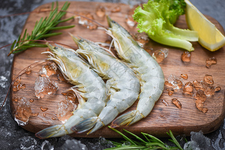 海产食品餐厅冰冻的生虾配有迷香成分药草和烹饪海鲜香料的木制剪板上新鲜虾背景图片