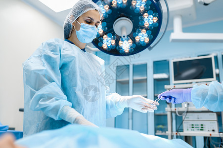 手术室背景灯外科手术穿制服的医生门诊药和保健手术室穿礼服和戴面罩的女外科医生手术刀高清图片素材