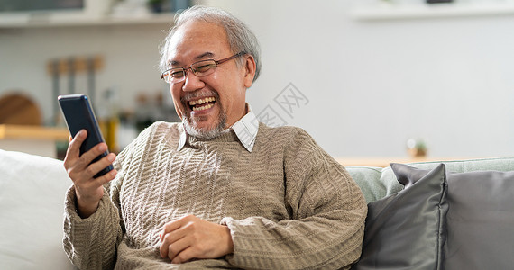 坐在客厅沙发上的年长男子使用手机带着笑和容给家人打视频电话图片