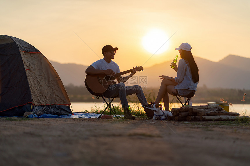 亚洲年轻成人夫妇在日落时帐篷露营地边弹吉他和喝啤酒图片