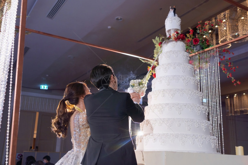 欢乐的亚洲夫妇在酒店礼堂的婚仪式上亲吻和新娘切蛋糕爱人们的结婚庆典图片