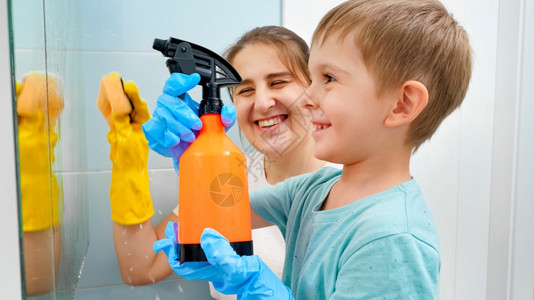 上洗手间男孩儿童小男孩在与母亲一起清洗浴室镜子时用喷洒的化学洗涤剂喷洒儿童小男孩在家中做务和清洁儿童小男孩在与母亲一起洗浴室镜子时用喷洒的化背景