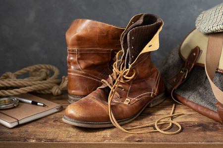 复古学生靴子旧皮革旅行靴鞋和木制桌布袋有墙背景纹理背景