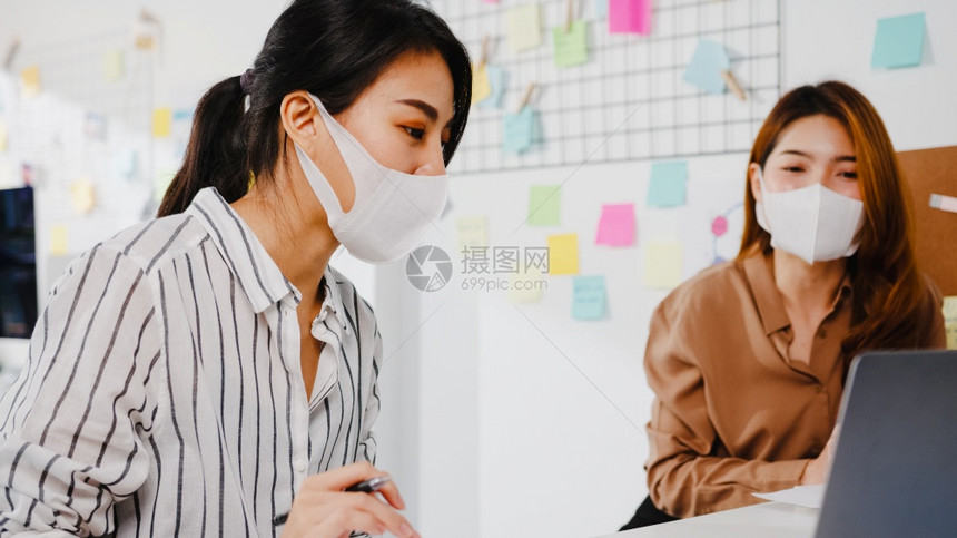 亚洲商界人士利用计算机演示集思广益地考新的项目同事并在新的正常办公室戴保护面罩图片