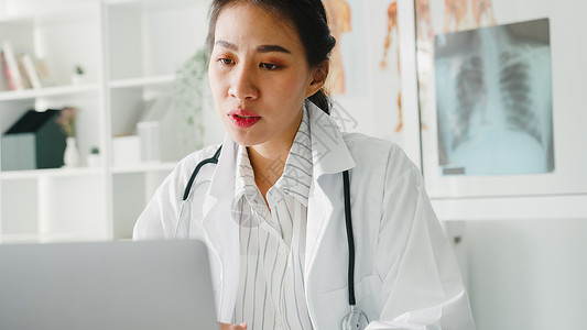 白制服听诊器的亚洲年轻女医生使用电脑笔记本交谈视频话在诊所或医院的服务台与病人通话采访高清图片素材