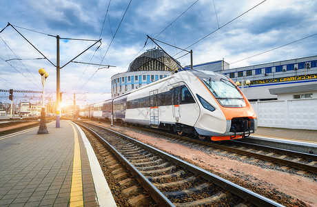 日落时火车站高速工业景观在铁路平台建筑物上移动现代城市间客运列车背景图片