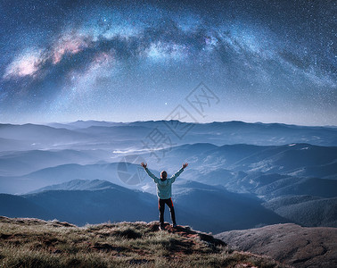 月星家居在山顶上欢乐的男子在山顶上横跨脉的银河在夜晚低云的中蓝天空的风景与星银河拱门小伙子雾中的山丘空间和星系空与恒的天背景