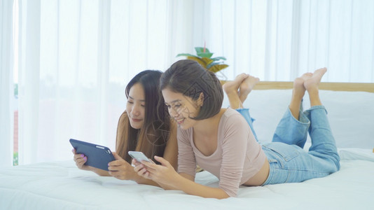 快乐的亚洲女青年孩躺在床上,家中卧室看平板电脑,学习技术设备概念。家庭高清图片素材