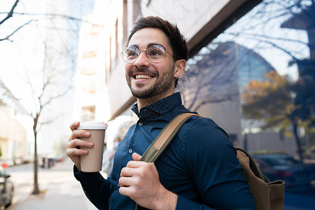青年男子在街上户外散步时拿着咖啡喝的肖像城市和生活方式概念背景图片