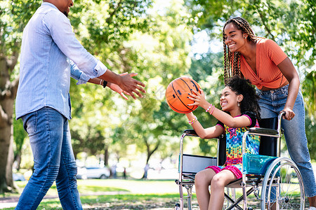 打篮球的女孩坐在轮椅上的小女孩在公园和家人一起享受打篮球背景