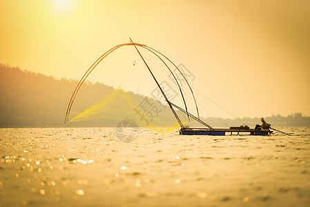 亚洲渔网利用木船在河上投下净日落或的木船侧影鱼网海上有山地岛屿背景的侧影鱼网背景图片