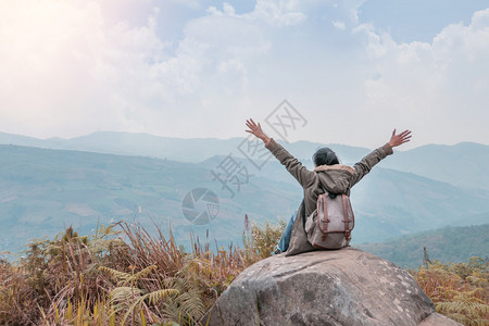 穿着背着包的坐在山顶岩石上与天空的蓝色相对高清图片