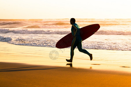 冲浪者在海滩上奔波日落时浪在葡萄牙背景图片