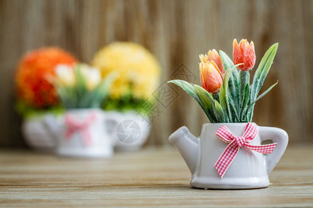 白色瓷锅中的人工郁金香配有茶壶设计和木本面粉红色丝带图片