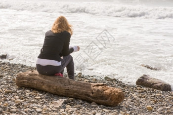 女孩坐在海边的日志上看着海图片