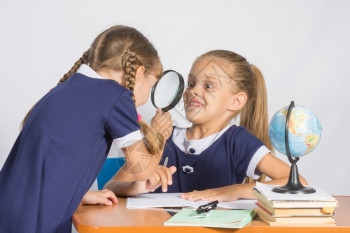 女孩在地理课上用放大镜看着另一个女孩图片