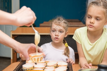 两个女孩惊讶的看着妈妈倒在模具上做蛋糕图片