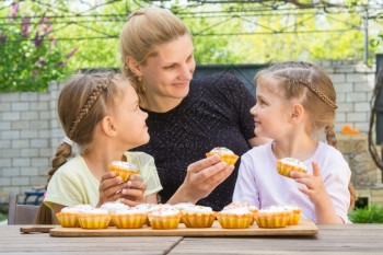 母亲和两个女儿坐在桌边拿着做好的蛋糕开吃图片