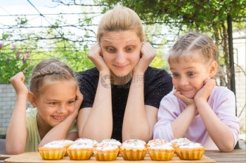 母亲和两个女儿有着不同表情看着纸杯蛋糕图片