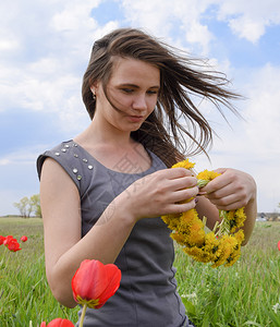 郁金香领域一位手拿着花圈的女孩一位在郁金香花丛中的美丽仙女年轻孩一位身着红花和绿地背景的女孩肖像一位脚印着红花和绿地的女孩背景