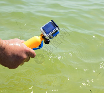 男人的手在水下盒子里拿着一个动作相机因为拍摄海面背景图片