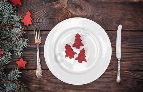 圆白陶瓷板和古老的叉子刀放在棕色木背景上边观绿色树枝配有圣诞装饰图片