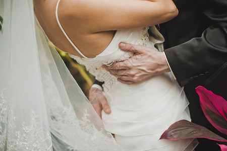 男人拥抱着穿白色裙子的女人腰部和底新娘的背图片