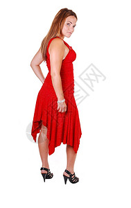 高跟鞋的可爱年轻女人站在工作室里穿着红色的裙子长棕头发仰望着肩膀图片