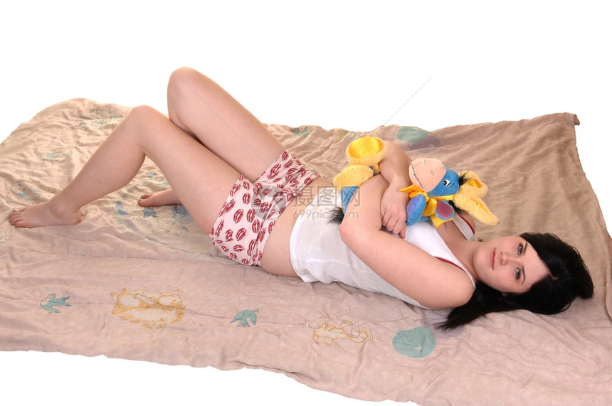 一位年轻美女躺在床上穿着睡衣躺在地上她的小床玩具笑着寻找白色背景图片