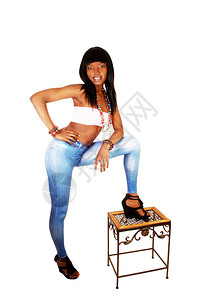 一个穿蓝色紧身裤的漂亮黑人女长的黑头发站在白地着一只腿在张小长凳上图片