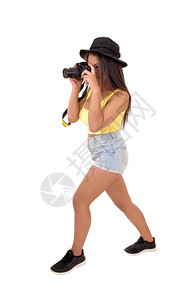 一个穿着短裤和帽子的年轻女站在摄影棚里拿着相机拍照图片