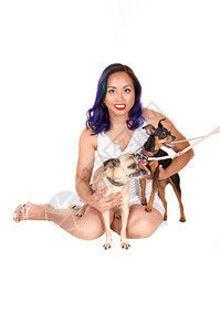 一位坐在地上漂亮的亚洲妇女抱着她的两只小狗在手臂上图片