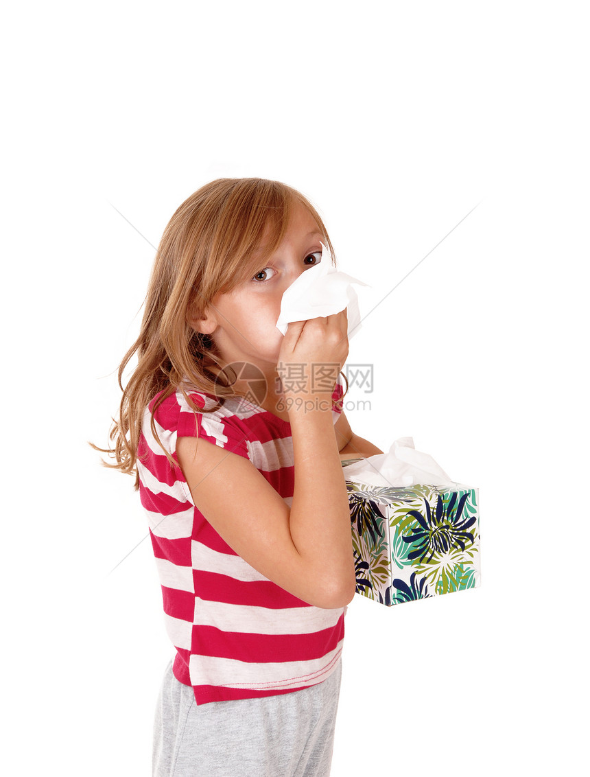 一个可爱的金发年轻女孩拿着一个组织在她跑鼻子上孤立的白色背景图片
