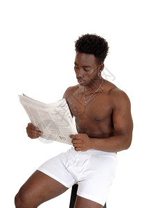 一个年轻的非裔美国人坐在椅子上穿着白内衣读报纸被白背景隔离背景图片