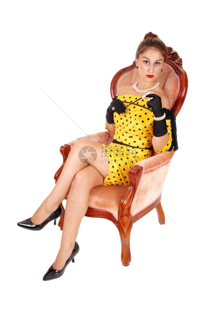 一位可爱的年轻女子穿着黄色礼服坐在粉红色的扶手椅上拿着长的烟筒与白种背景隔绝图片