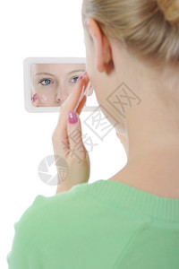 美貌丽的女人在镜子前脸颊上施奶油背景图片
