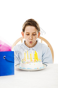 小男孩在生日蛋糕上吹蜡烛白色背景图片