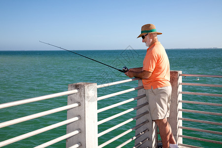 顶草帽的老人在码头上钓鱼进入大海图片