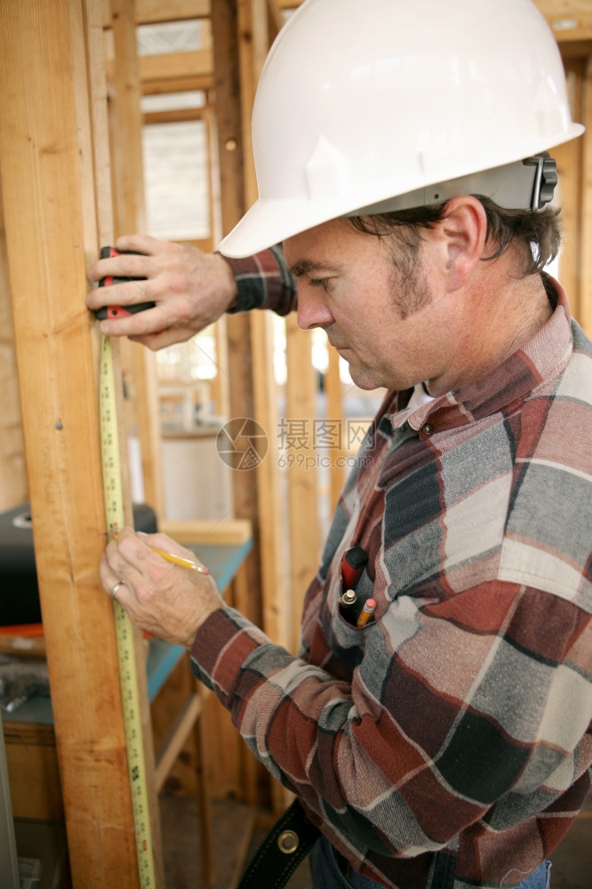 建筑工人在地测量木束的垂直视图以他的脸为焦点图片