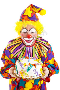 有趣的小丑在生日蛋糕上吹蜡烛白纸孤立背景图片