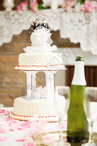 婚礼蛋糕装饰着两个新郎在接待台与香槟和玫瑰花瓣图片
