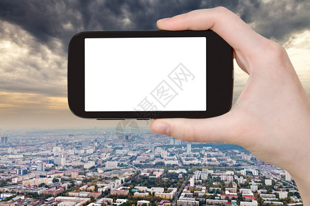 旅行概念手持智能机用剪的屏幕和风暴云挡住城市背景图片