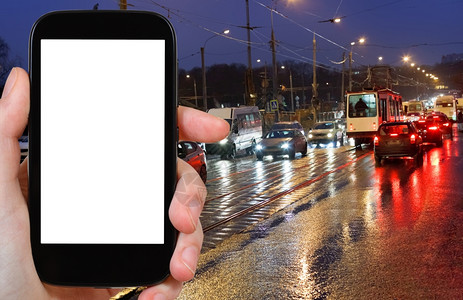 旅行概念手持智能机在夜里按背景截断屏幕在城市街道上湿透图片