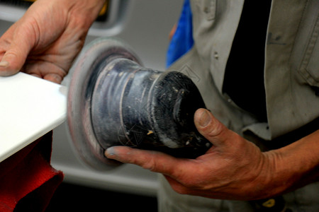 男子在汽车修理间用磨机在汽车零件上磨砂图片素材