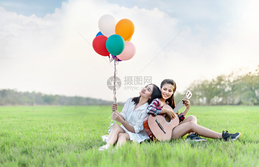 两个快乐的女人在绿田中放松快乐的漂亮女人带着气球图片